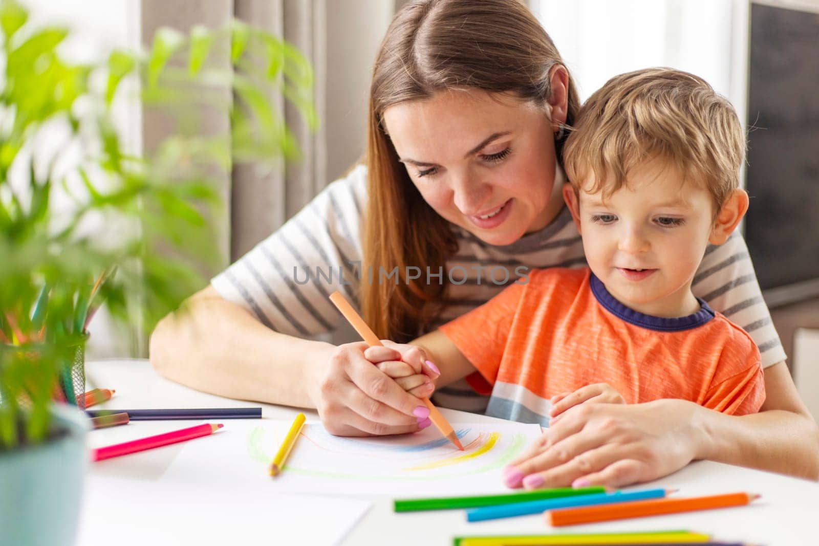 Mother and child drawing with pencils sitting at the desk at home. Happy family