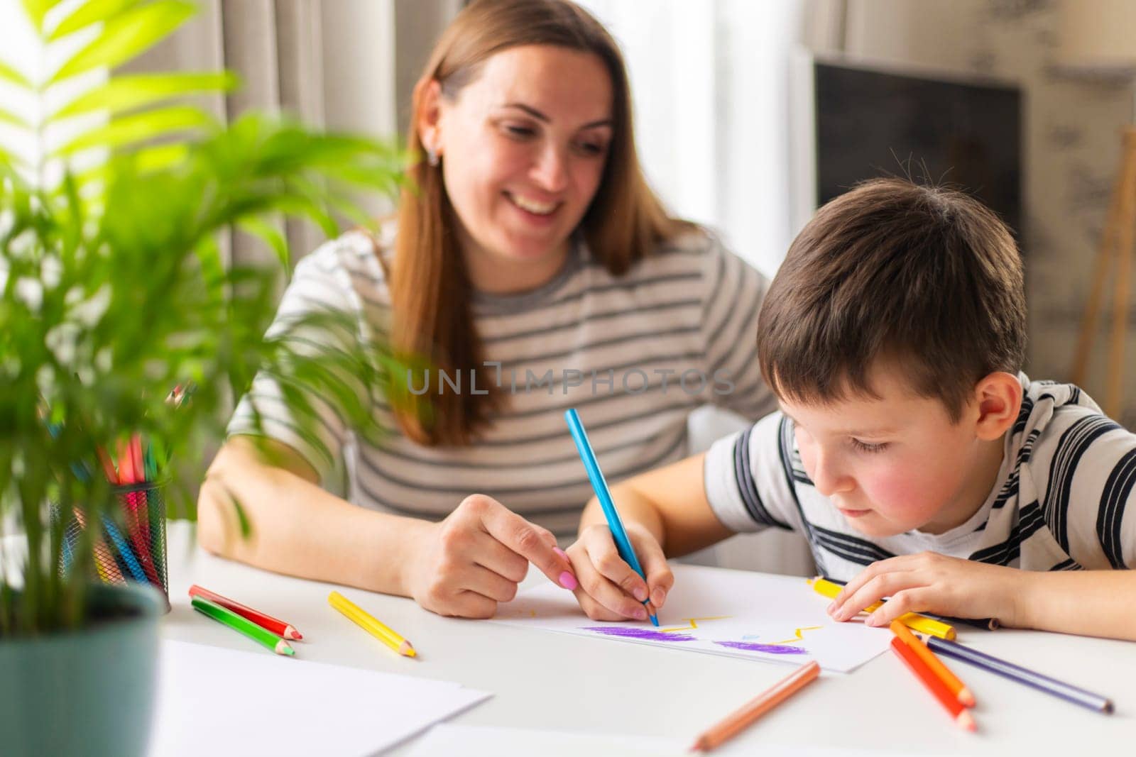 Mother and child drawing with pencils sitting at the desk at home. Happy family