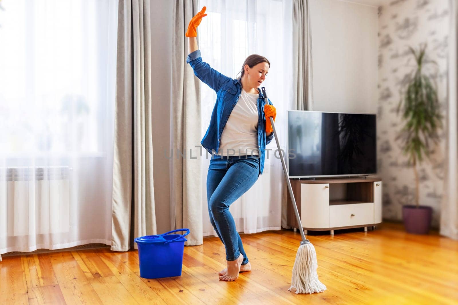 Funny happy young woman with mop singing, dancing and having fun while cleaning floor. Housewife enjoying domestic chores, doing home cleanup creatively