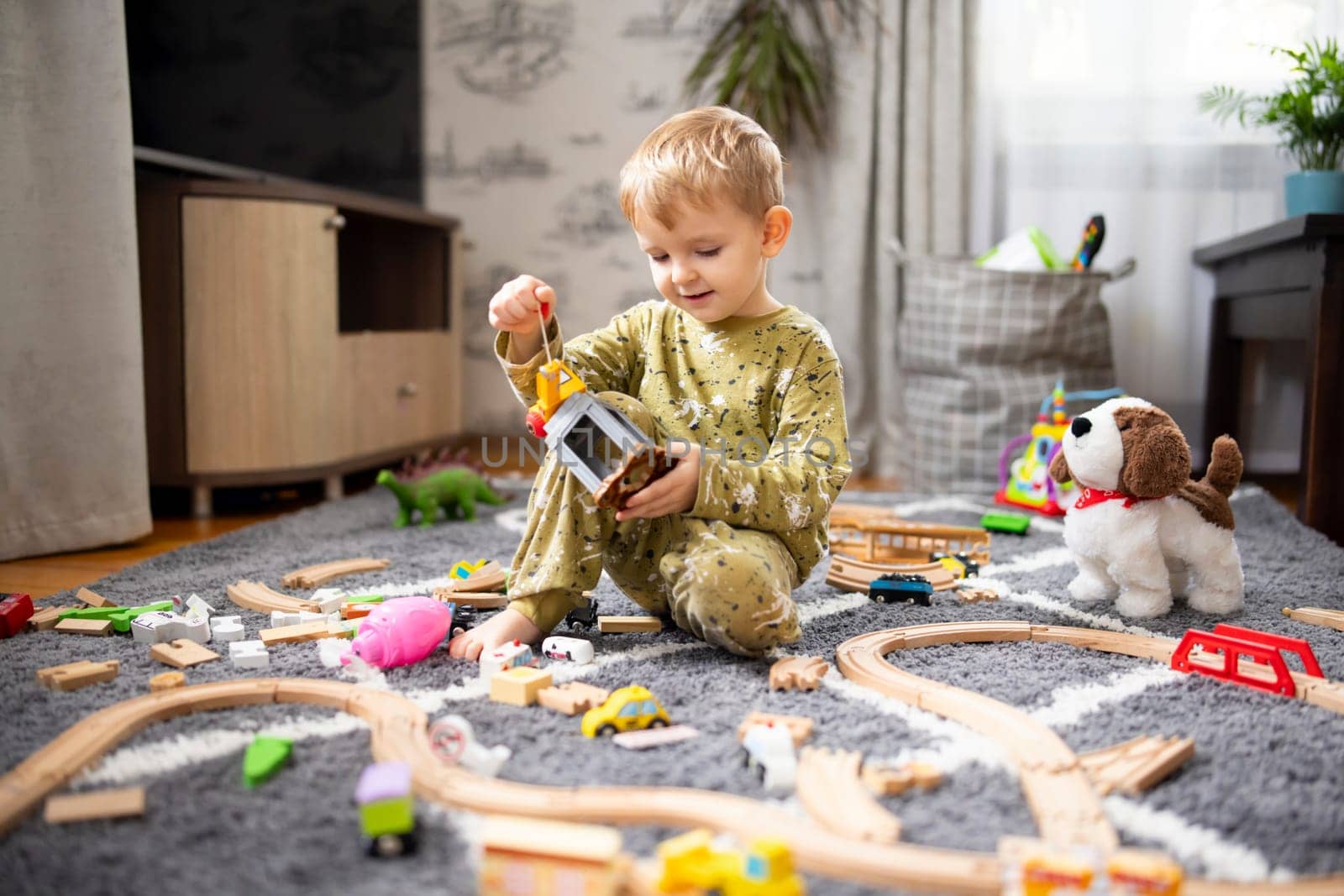 Child playing with developmental toys. Baby playing with toy railroad, trains and cars on the floor. Children at home or in kindergarten