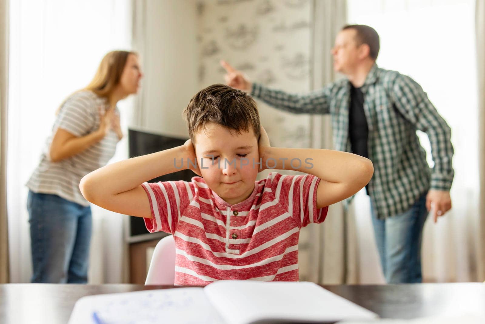 Sad child covers his ears with his hands during an argument between his parents by andreyz