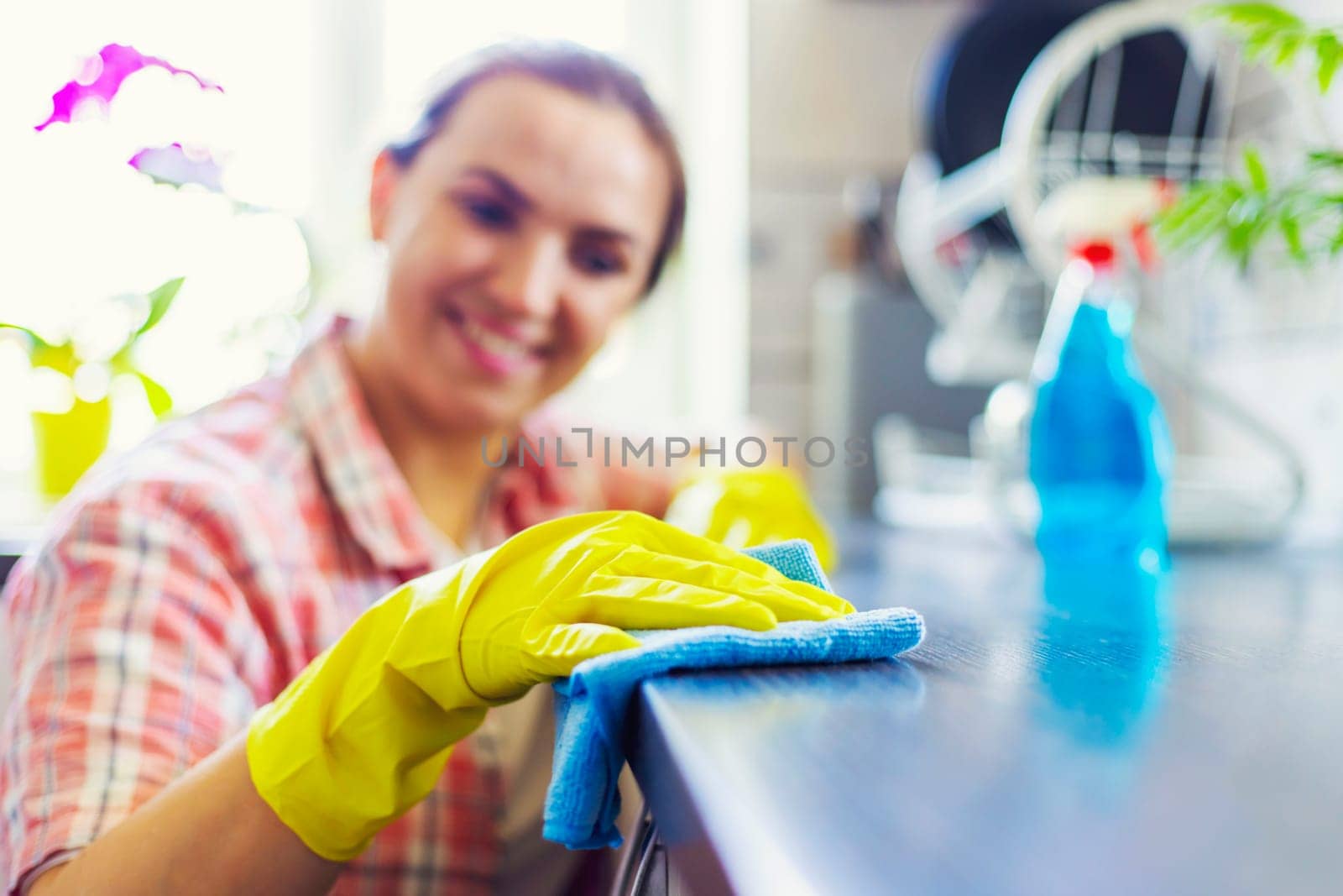 Housewife in yellow gloves wipes dust using spray detergent and rag. The woman is doing household chores. Cleaning concept