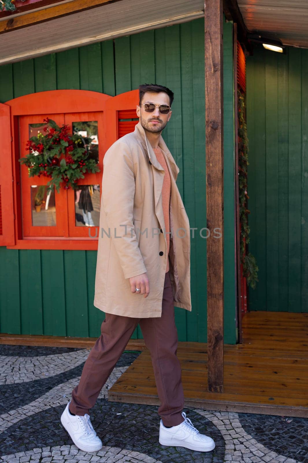 Handsome man in trendy outfit walking near Christmas house by andreonegin
