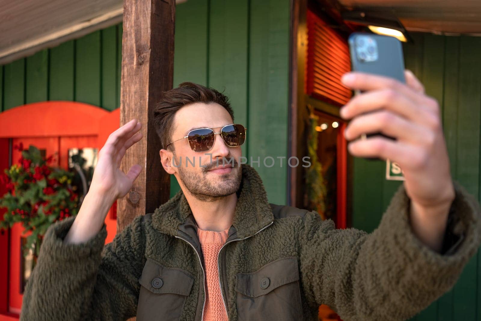 Man in trendy jacket and sunglasses taking selfie with smartphone in city by andreonegin