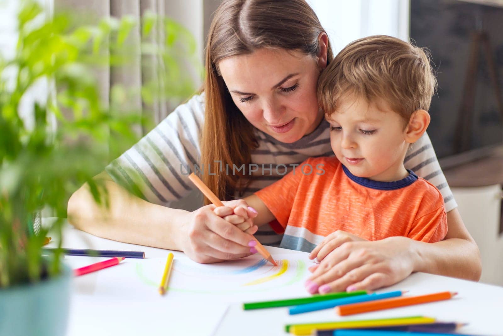 Mother and child drawing with pencils sitting at the desk at home. Happy family