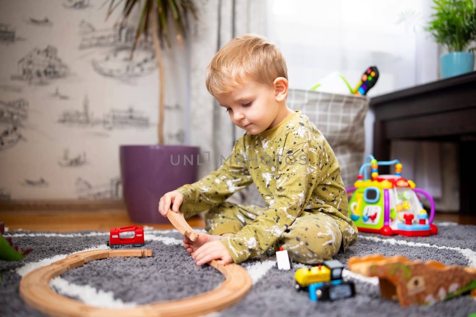 Child playing with developmental toys. Baby playing with toy railroad, trains and cars on the floor. Children at home or in kindergarten