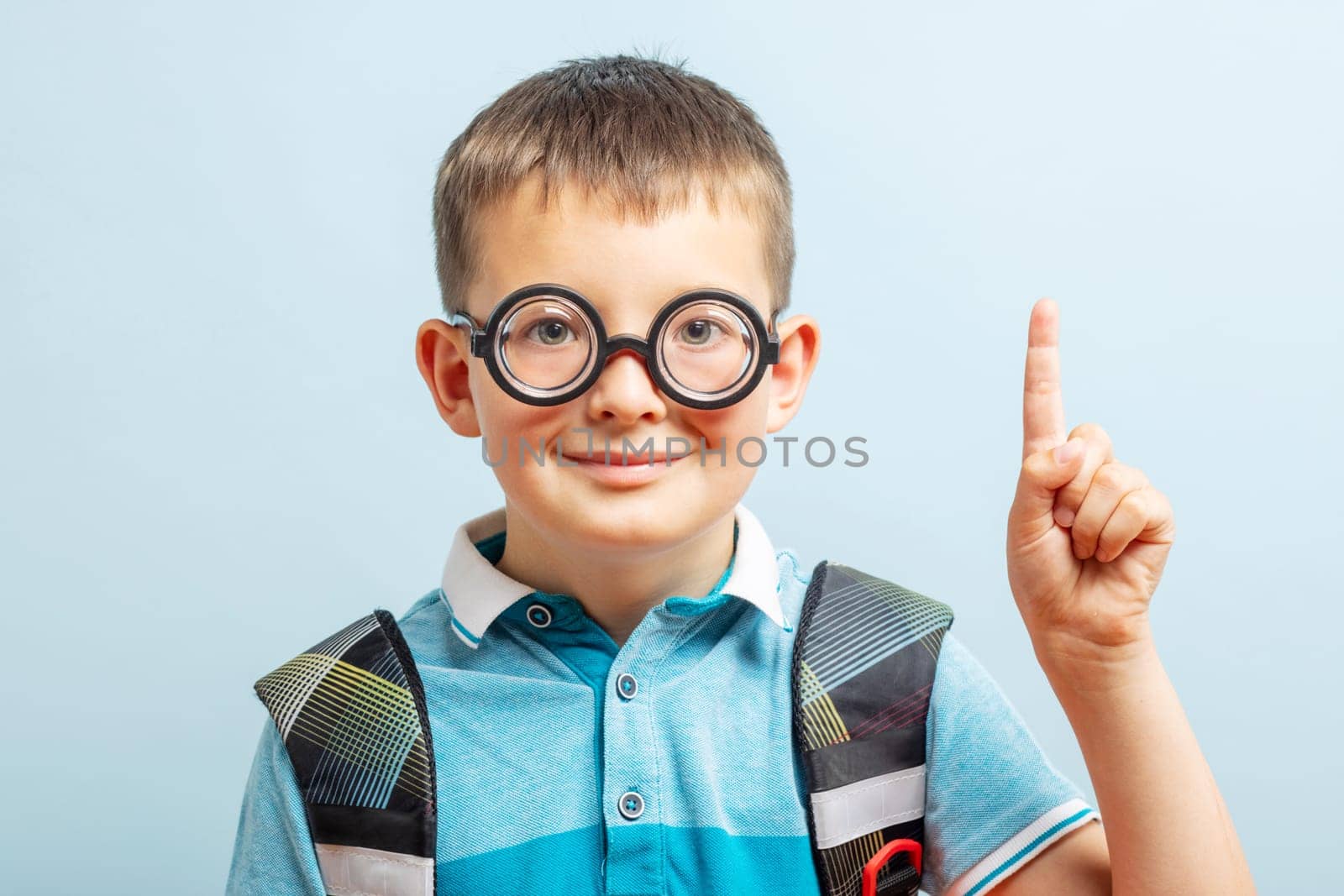 A cute school boy in glasses with raised index finger on blue background by andreyz