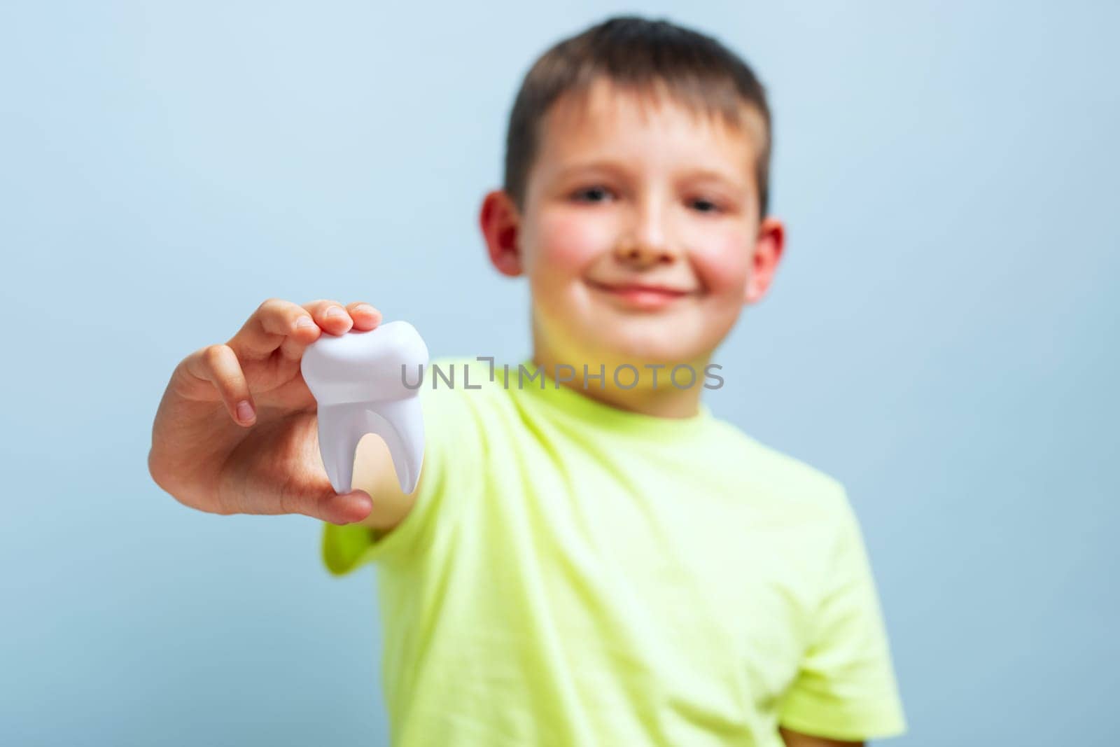 Child shows big white toy tooth on a blue background. Caring for teeth. Dentistry and healthcare concept. Healthy teeth concept
