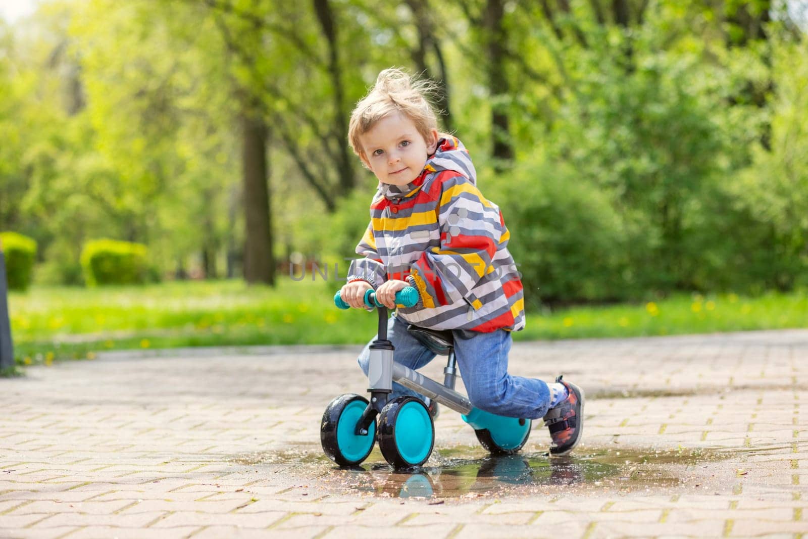 Active blond boy riding balance bike or run bike outdoor park. Active kid playing outside