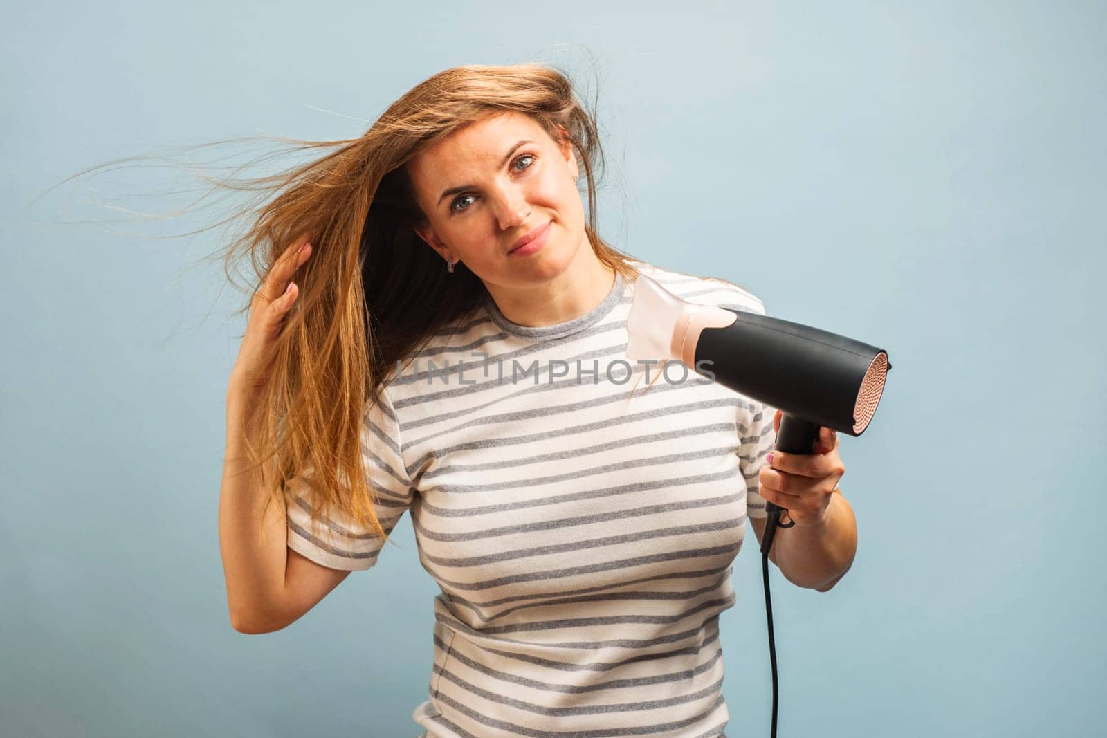 Young smiling woman using hair dryer on blue background. Hair style, hair care concept
