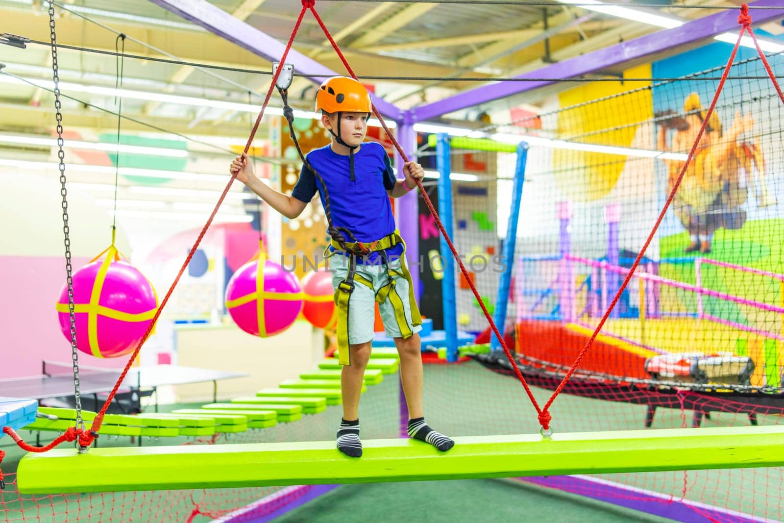 Boy in protective gear holding safety rope and passing obstacle course in indoor adventure park