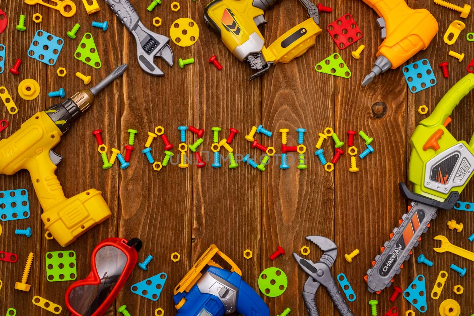 Colorful toy tools, bolts and nuts as frame with text WORKSHOP on wooden background. Top view. Flat lay