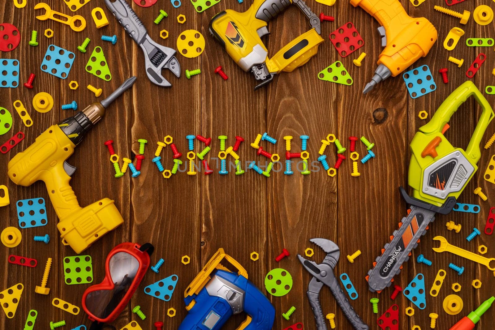 Colorful toy tools, bolts and nuts as frame with text WORKSHOP on wooden background. Top view. Flat lay