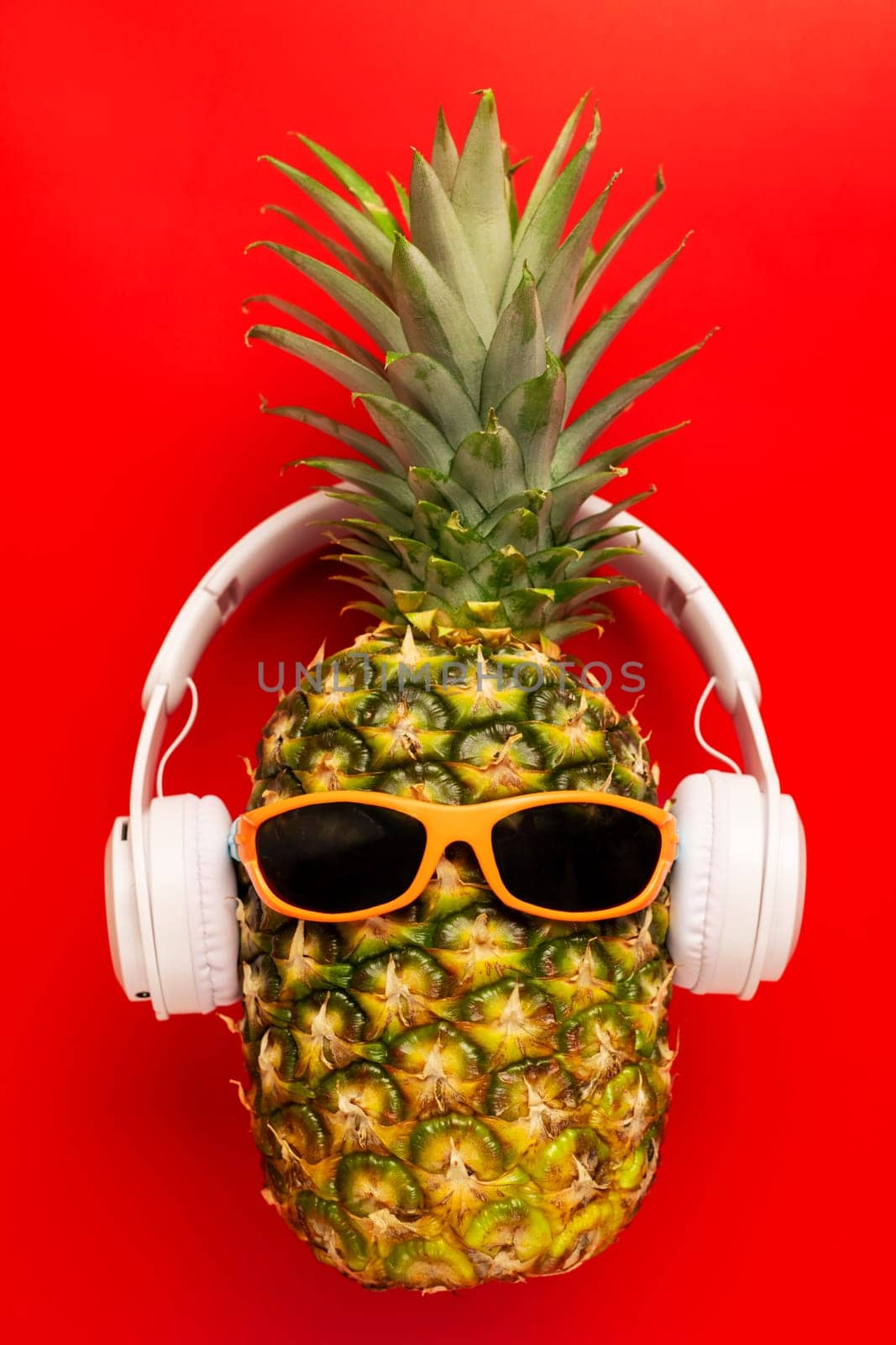 Ripe pineapple with sunglasses and headphones on red background. Copy space