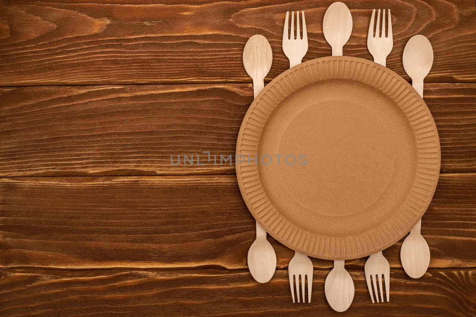 Wooden forks and spoons and paper plate on wooden background. Biodegradable eco-friendly dishes