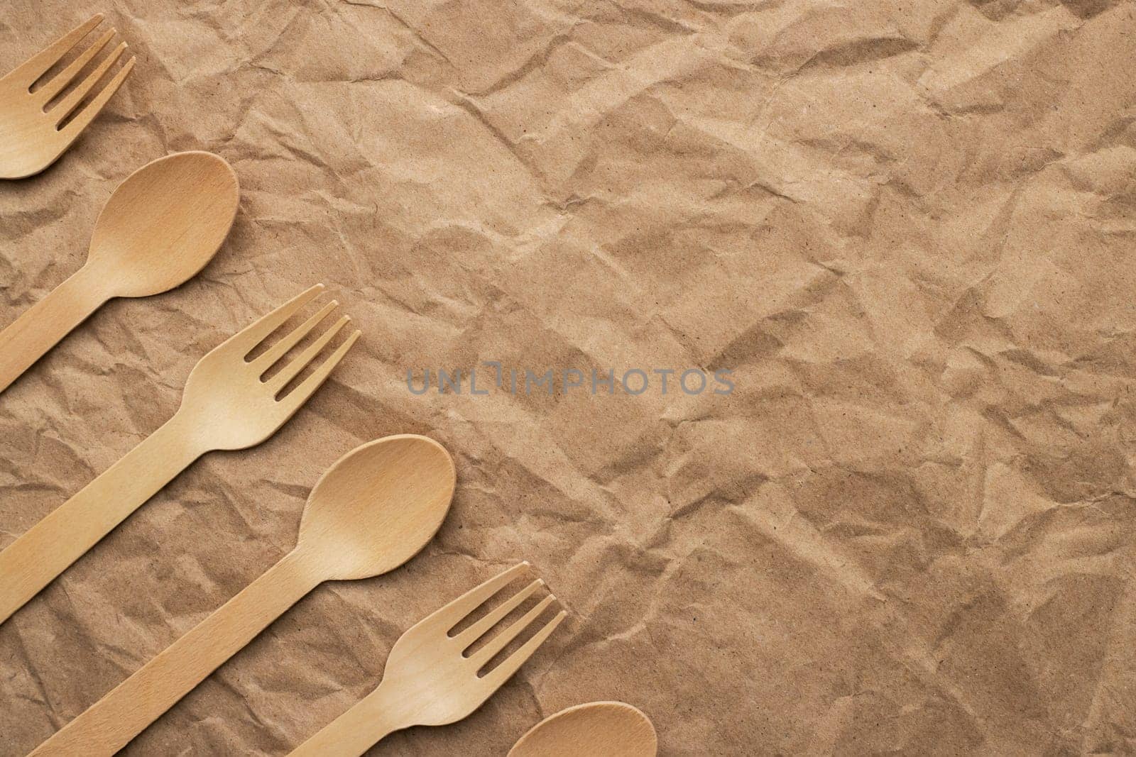 Set of wooden forks and spoons on crumpled paper background. Biodegradable eco-friendly dishes. Top view