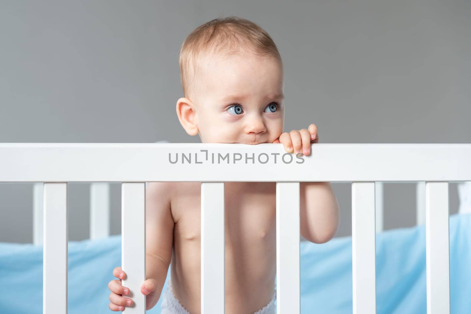 Happy baby playing in the crib, with a sweet smile, and gnawing on its side.