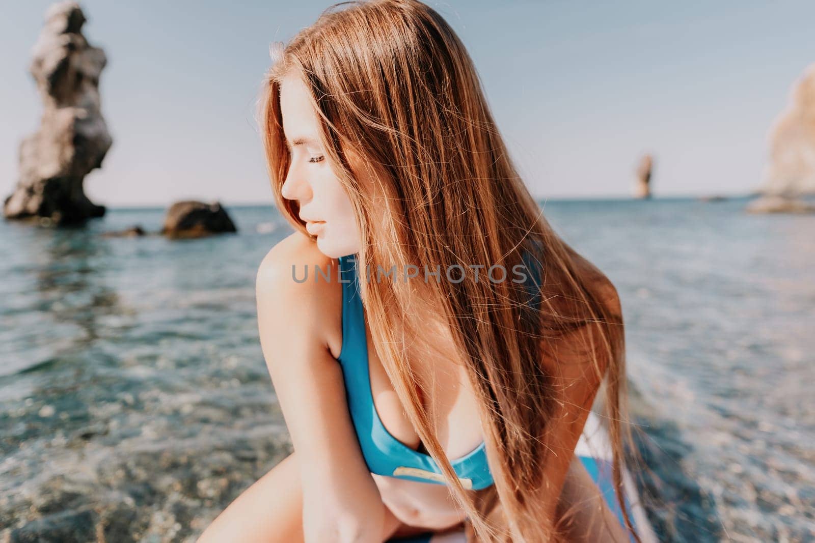 Close up shot of happy young caucasian woman looking at camera and smiling. Cute woman portrait in bikini posing on a volcanic rock high above the sea