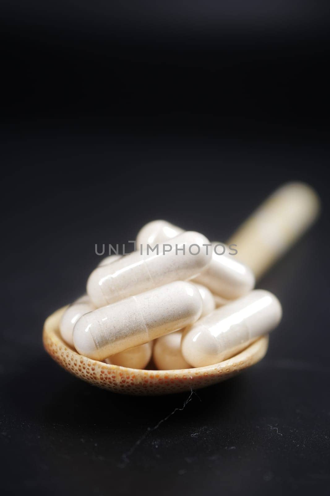 herbal medicine capsules on a spoon on black background .