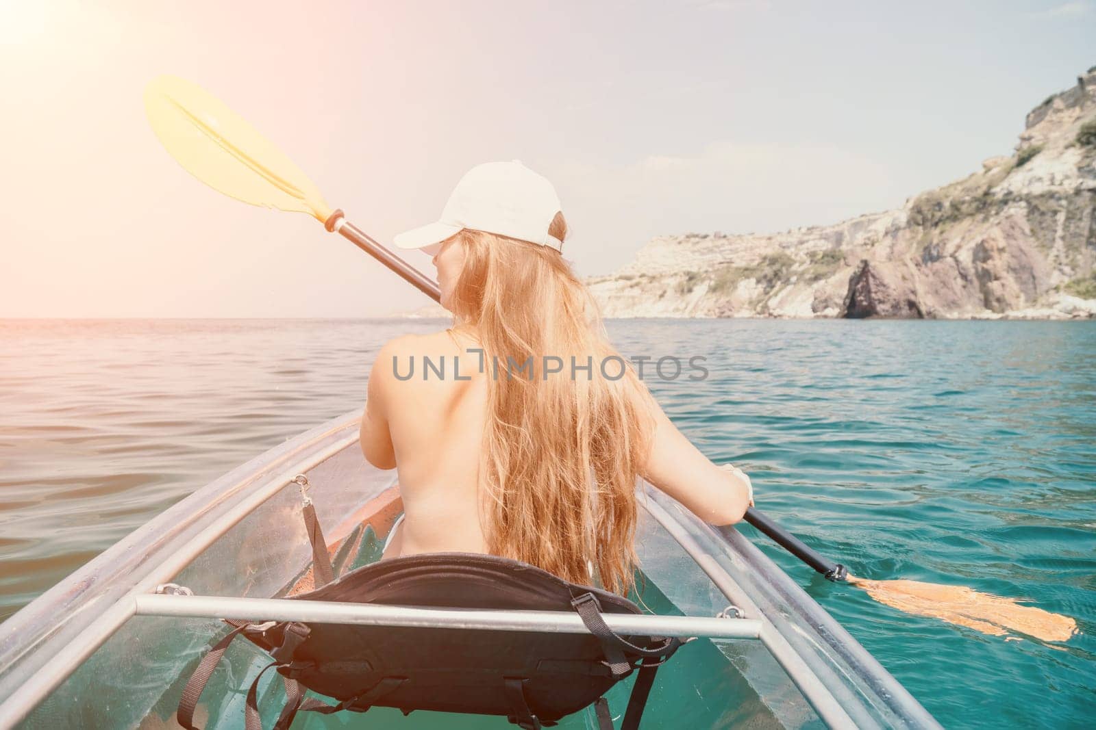 Woman in kayak back view. Happy young woman with long hair floating in transparent kayak on the crystal clear sea. Summer holiday vacation and cheerful female people having fun on the boat.