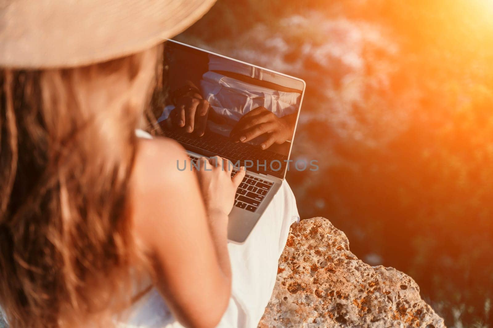 Freelance happy woman typing on her laptop, enjoying the picturesque sea view, highlighting the idea of working remotely with a relaxed and pleasant atmosphere