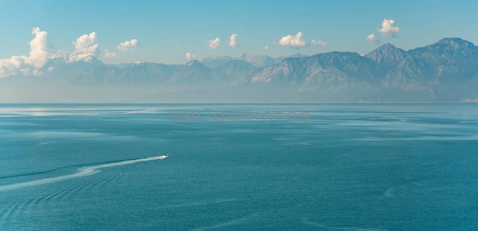 Antalya landscape with a boat sailing on the sea and mountains in the background by Sonat