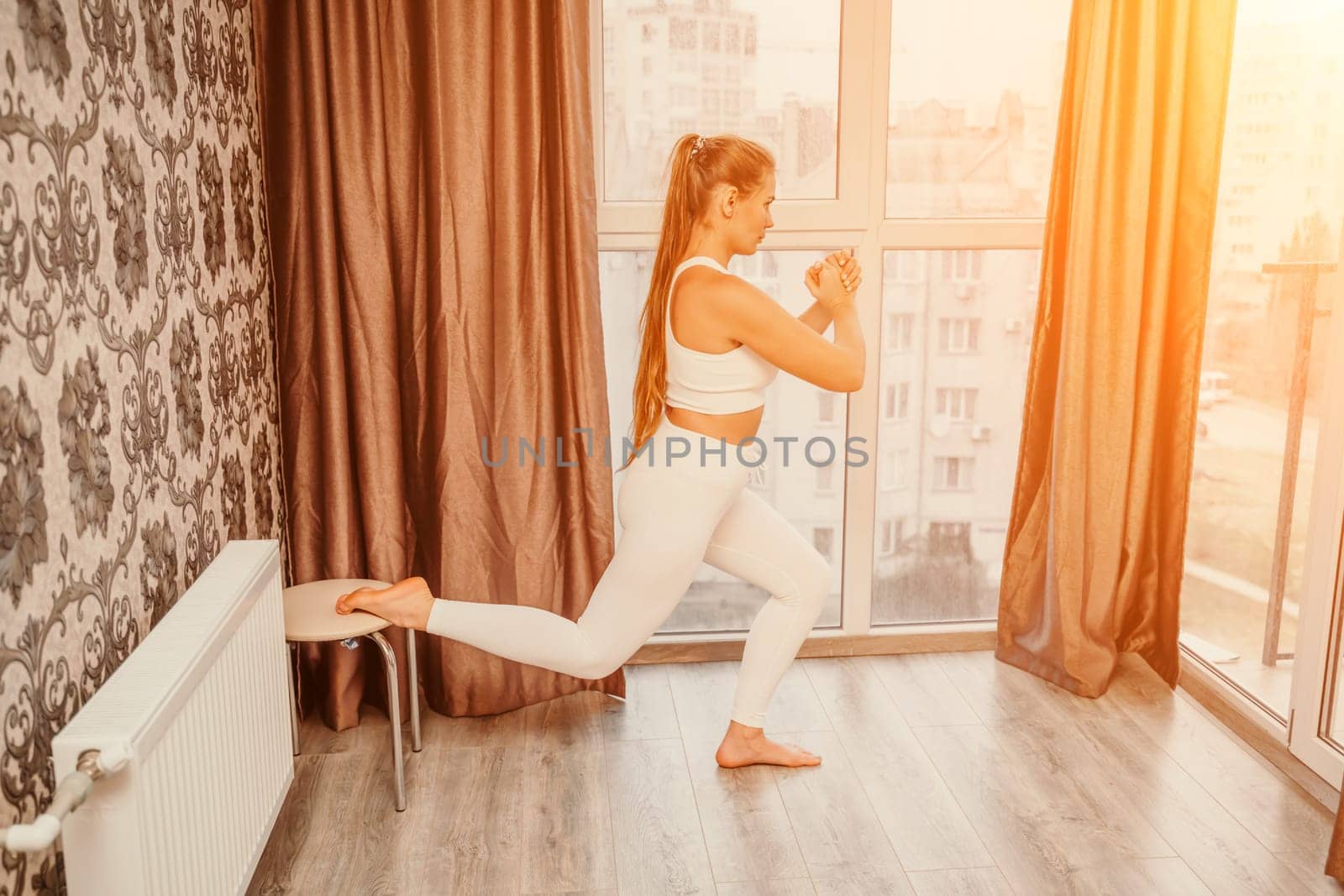 Middle aged athletic attractive woman practicing yoga. Works out at home or in a yoga studio, sportswear, white pants and a full-length top indoors. Healthy lifestyle concept by Matiunina