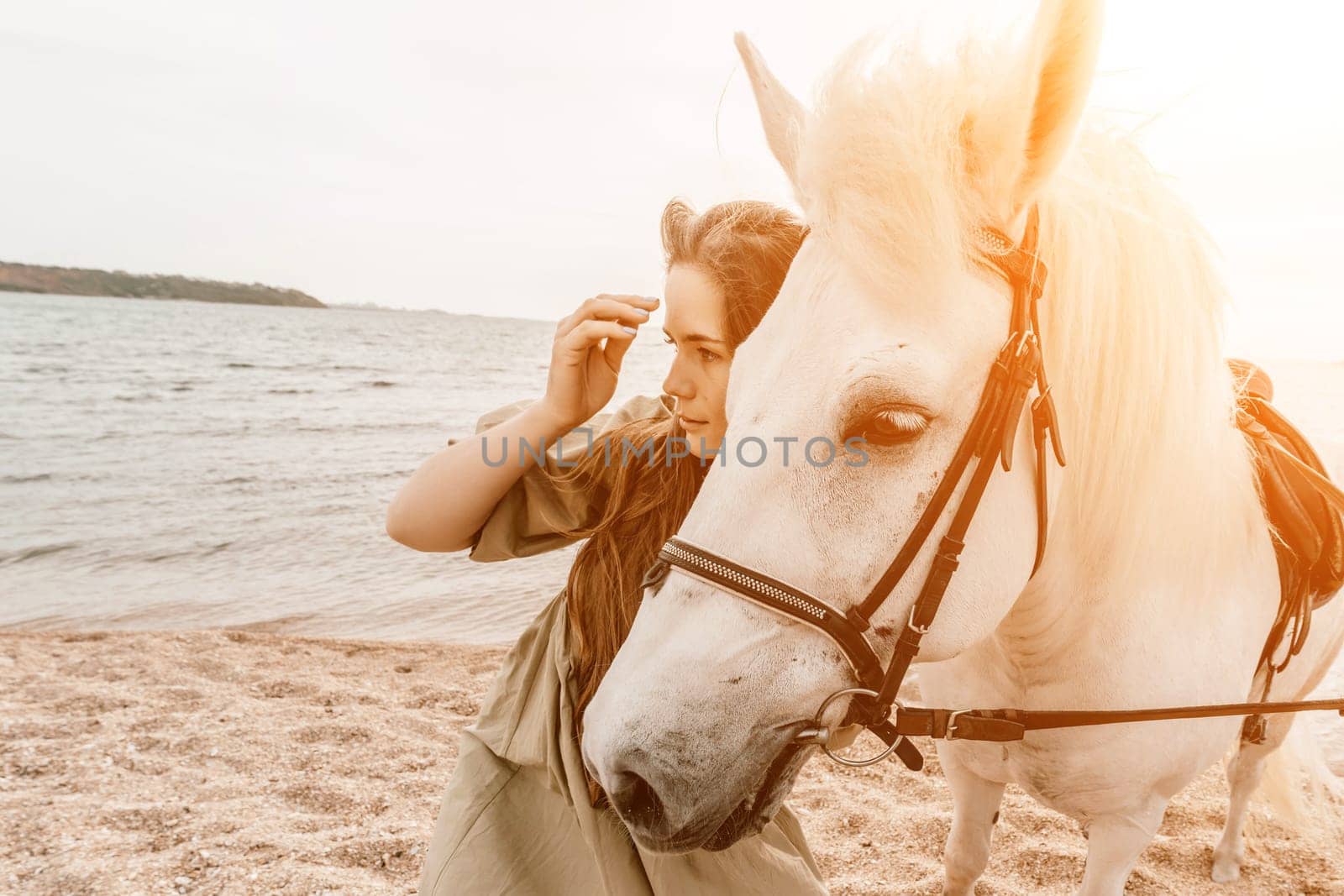 A white horse and a woman in a dress stand on a beach, with the sky and sea creating a picturesque backdrop for the scene