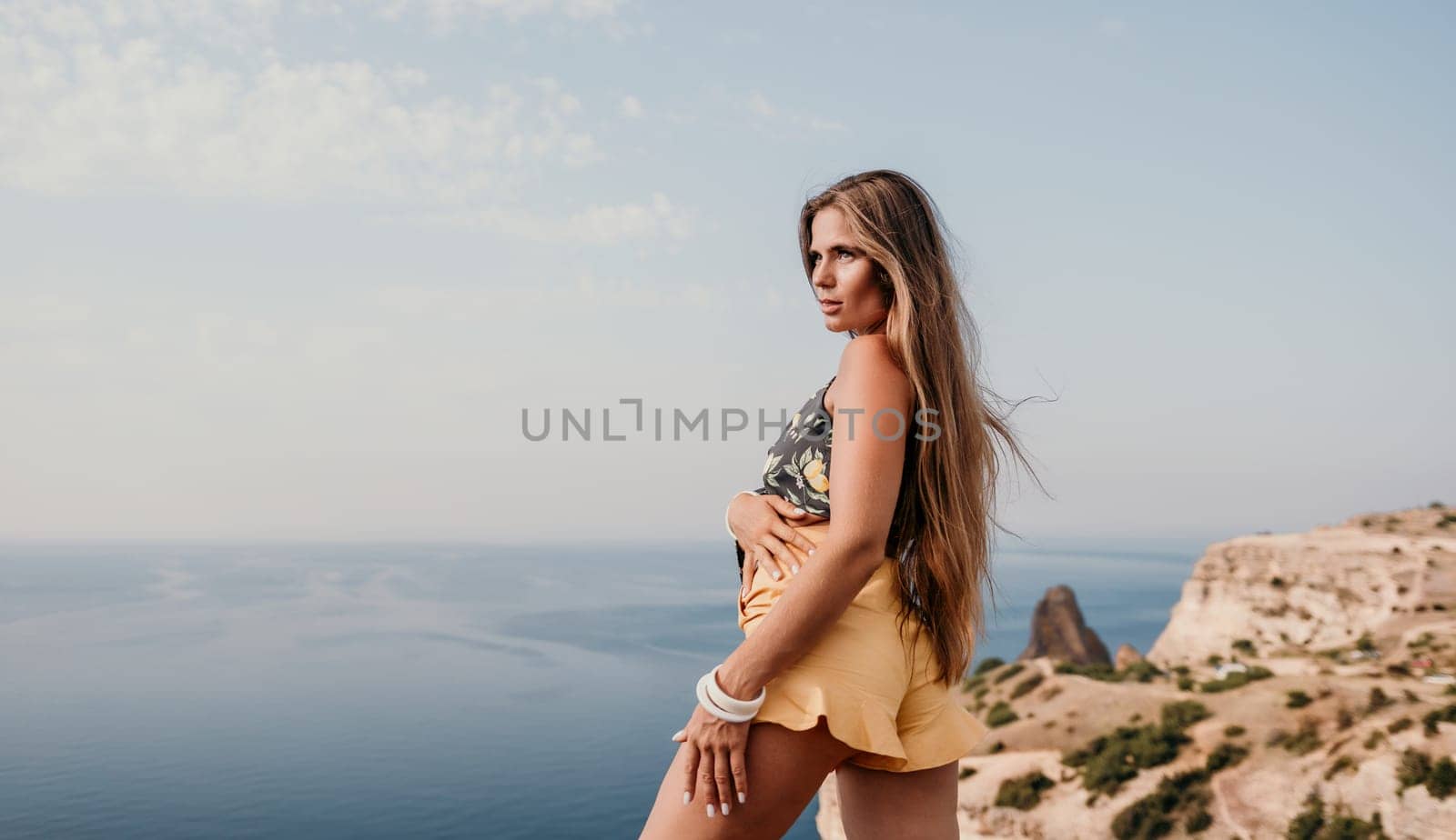 Woman travel sea. Happy tourist taking picture outdoors for memories. Woman traveler looks at the edge of the cliff on the sea bay of mountains, sharing travel adventure journey.