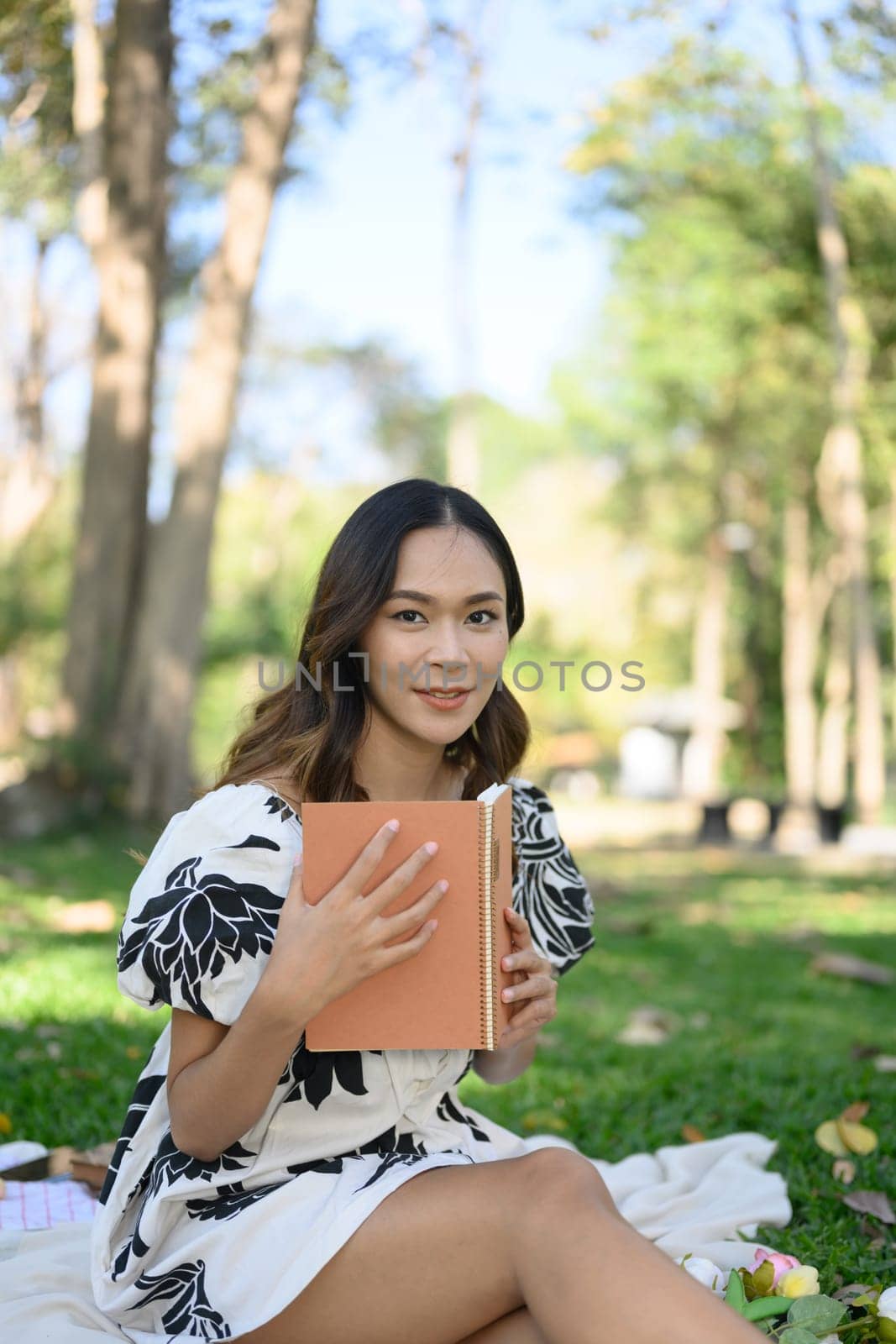 Portrait of charming young woman relaxing with the book during picnic in the park on the sunny day.