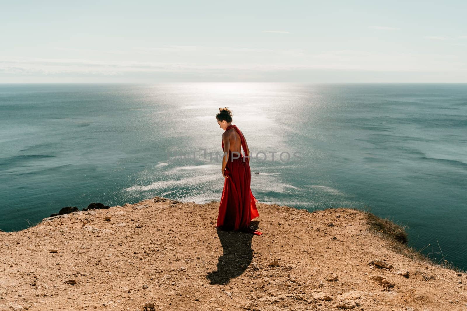 Woman red dress sea. posing on a rocky outcrop high above the sea. Girl on the nature on blue sky background. Fashion photo