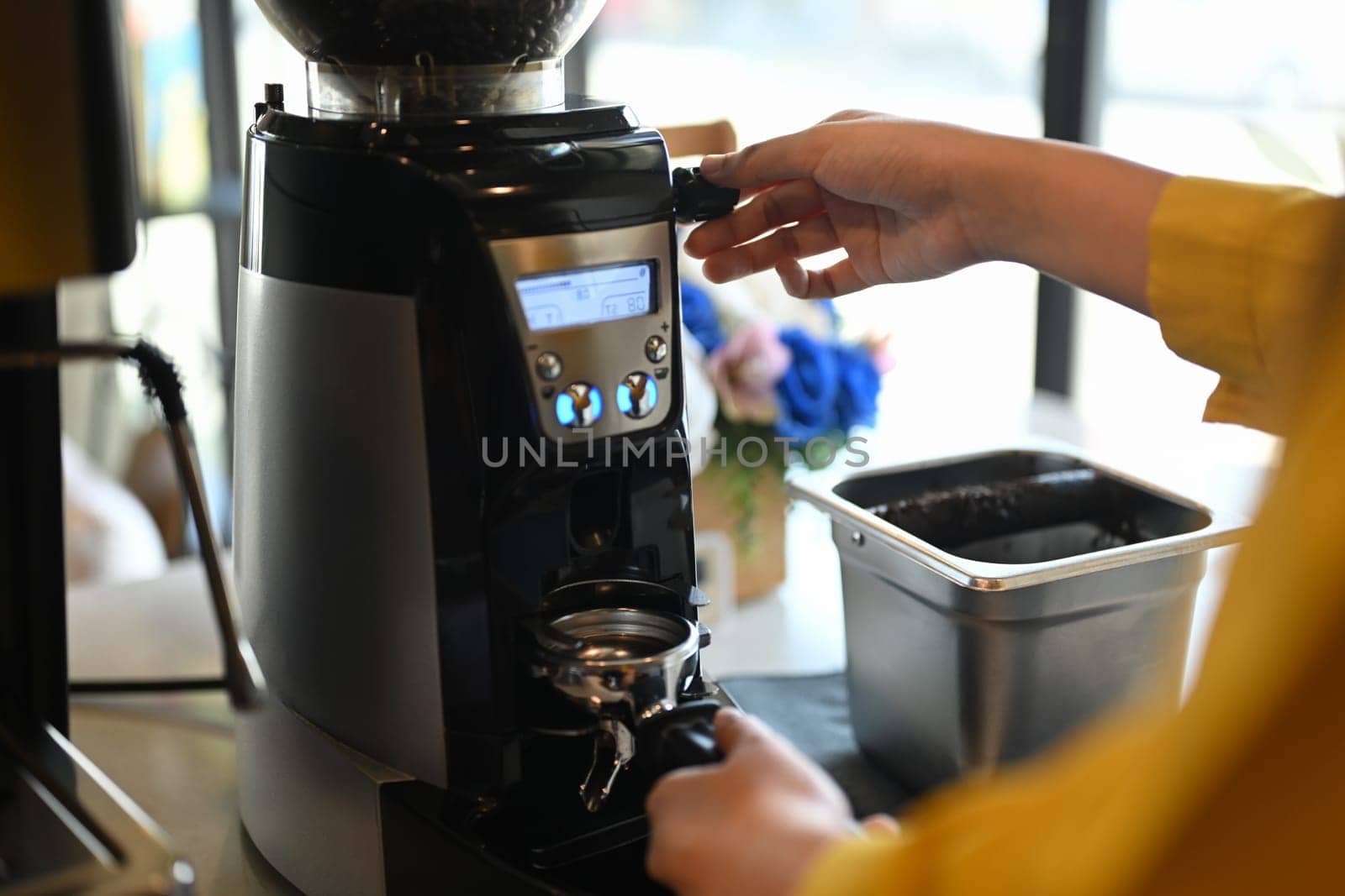 Barista using grinder machine to grinding fresh roasted coffee bean at modern coffee shop.