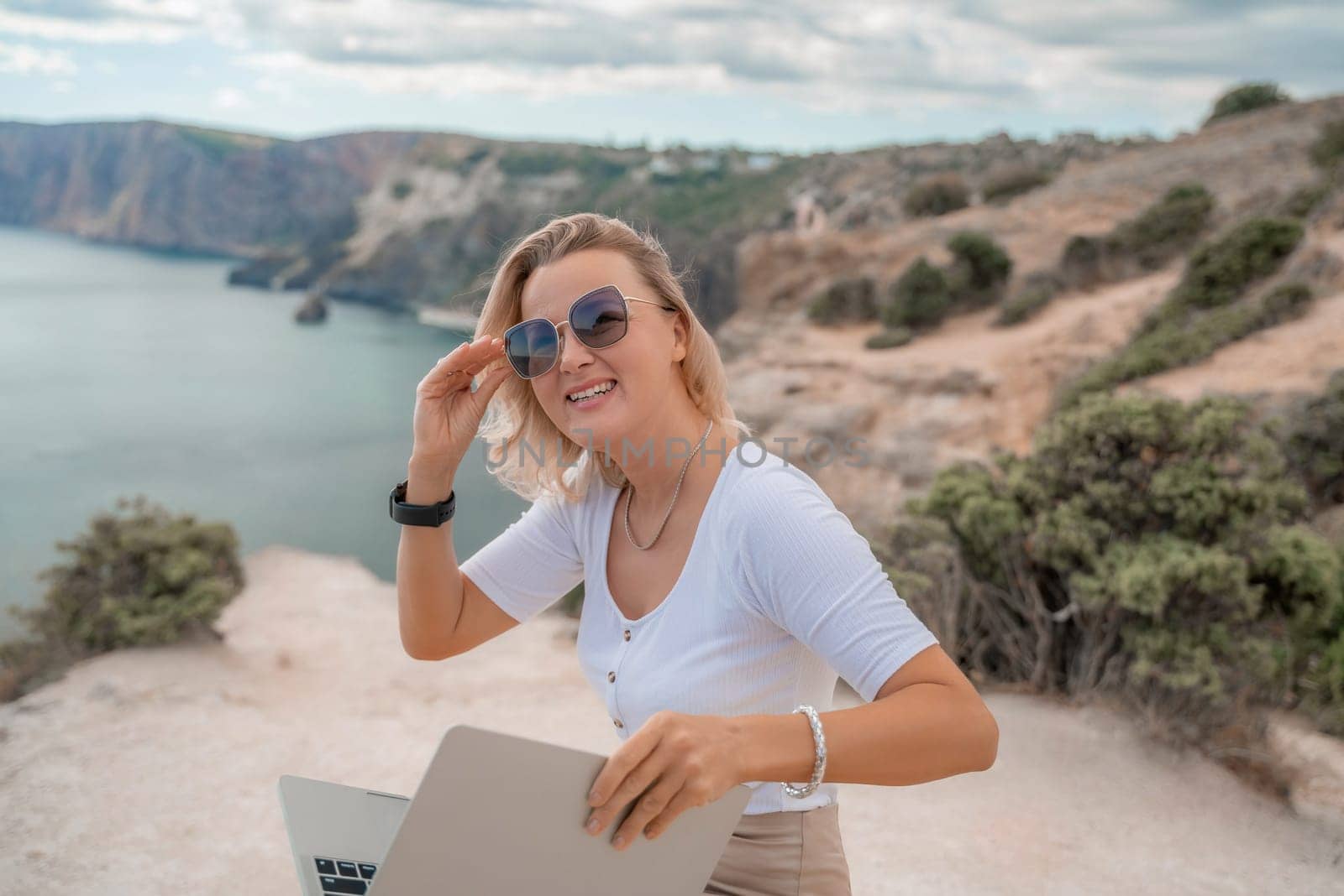 Freelance women sea working on the computer. Good looking middle aged woman typing on a laptop keyboard outdoors with a beautiful sea view. The concept of remote work