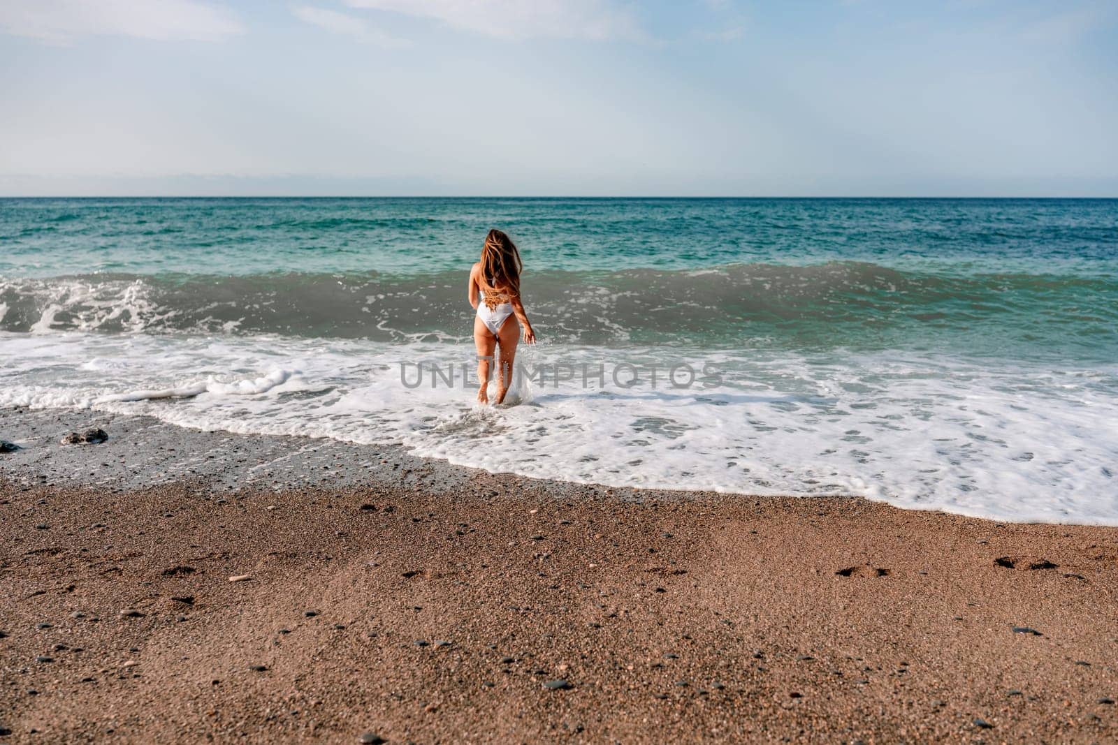 Happy woman in bikini running on the beach. Active leisure, a beautiful girl in a bikini is having fun on the beach, big waves are splashing along the beach