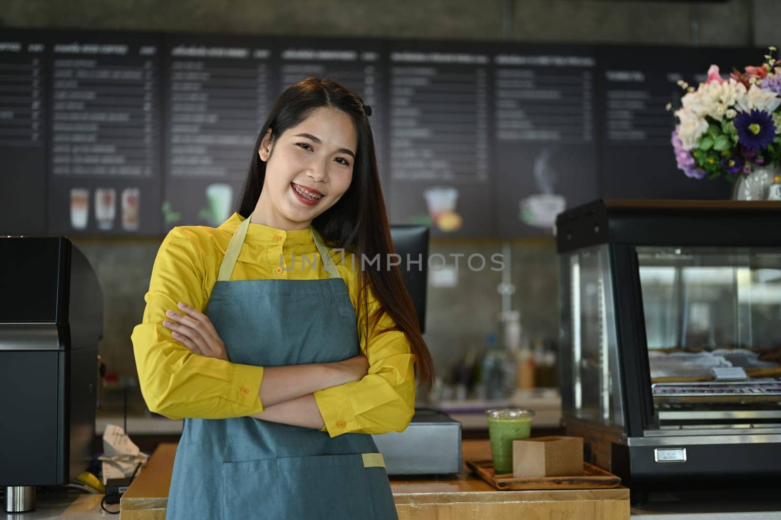 Portrait of confident small coffee shop owner standing with arms crossed at counter.