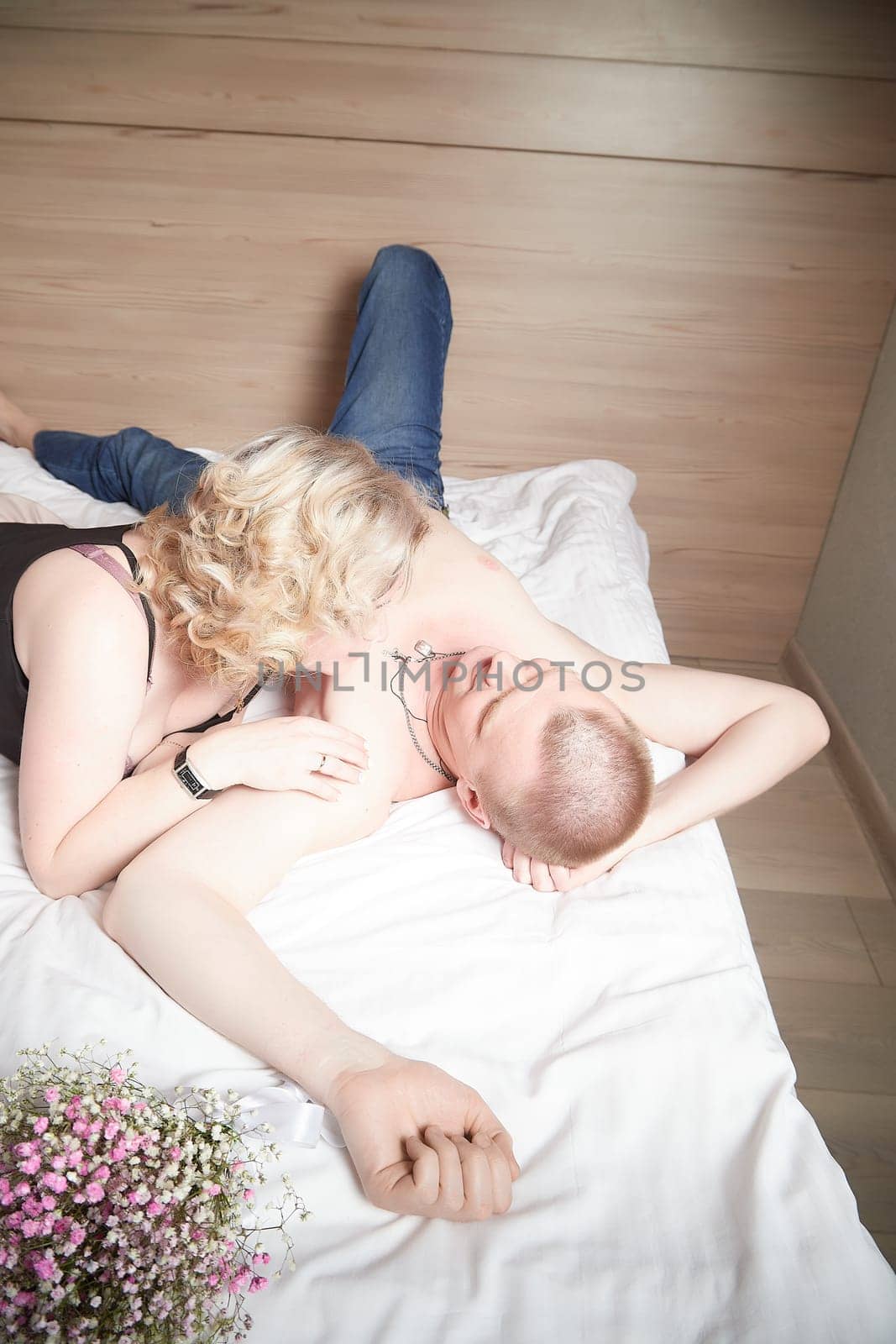 Loving enamored adult couple communicates, embraces, and has fun alone together on the bed in the bedroom or hotel room. The woman is wearing a tank top and the man is shirtless by keleny