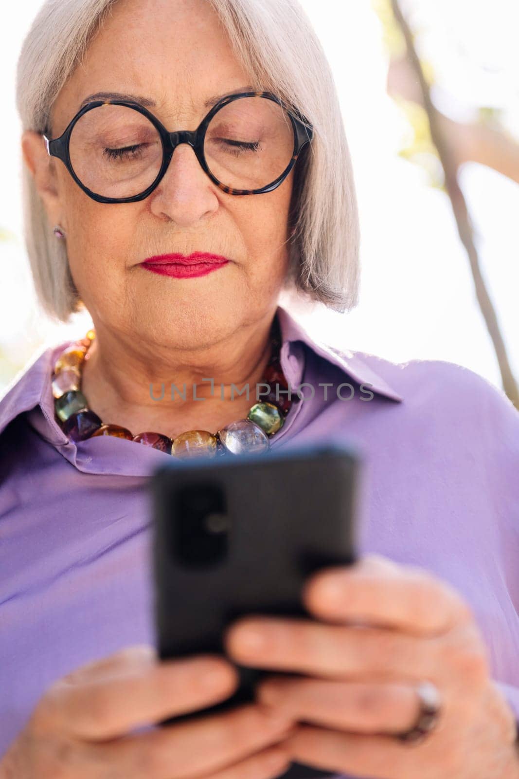 close up portrait of a senior woman using mobile phone on the street, concept of technology and elderly people leisure