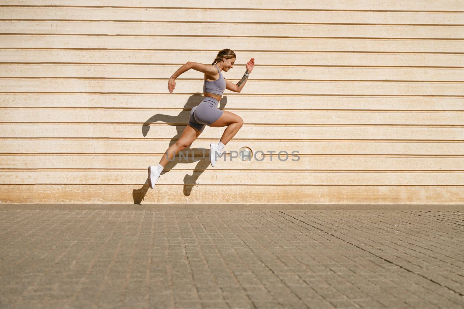 Female athlete in sportswear leaping in air with wall backdrop outdoors. Healthy lifestyle concept