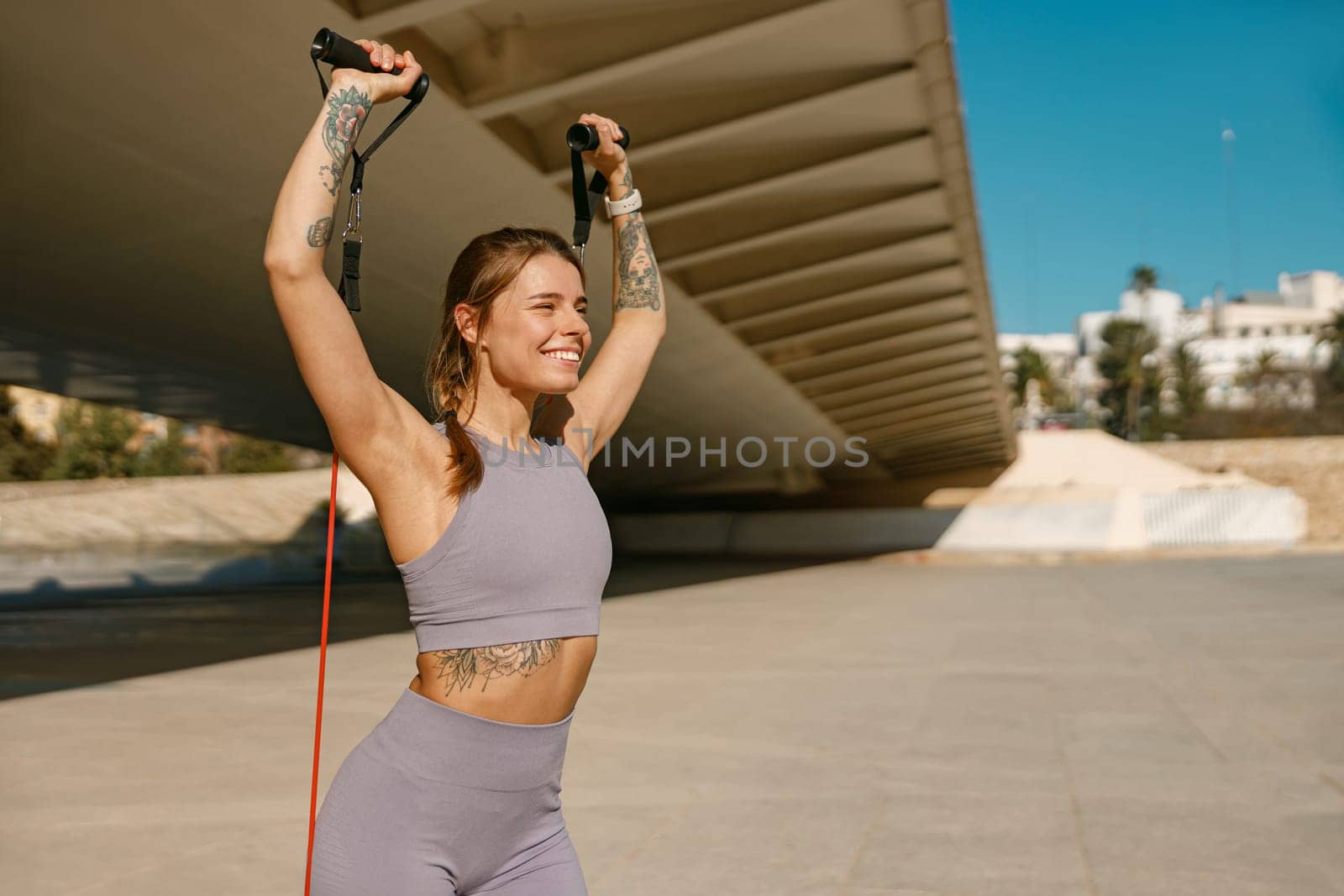 Fitness woman doing exercise with resistance elastic band outside in urban environment by Yaroslav_astakhov