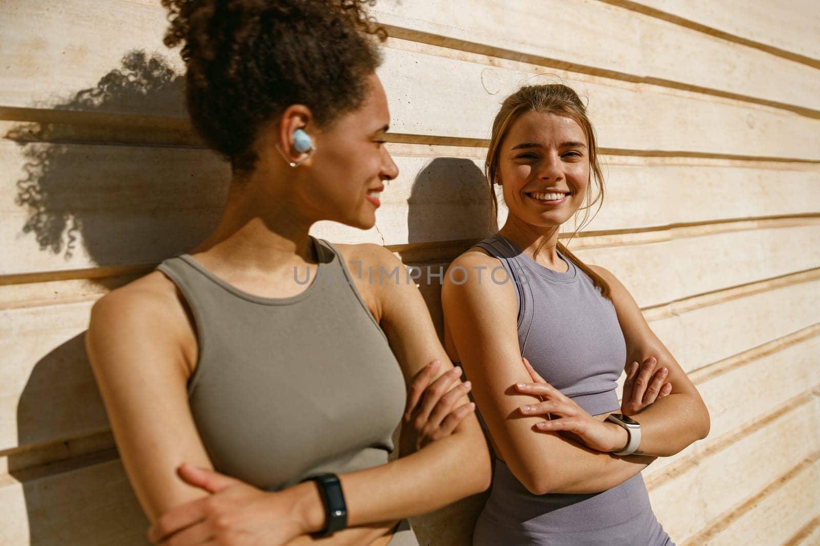 Smiling female sportswomen with crossed hands have a rest after morning jogging outdoors by Yaroslav_astakhov