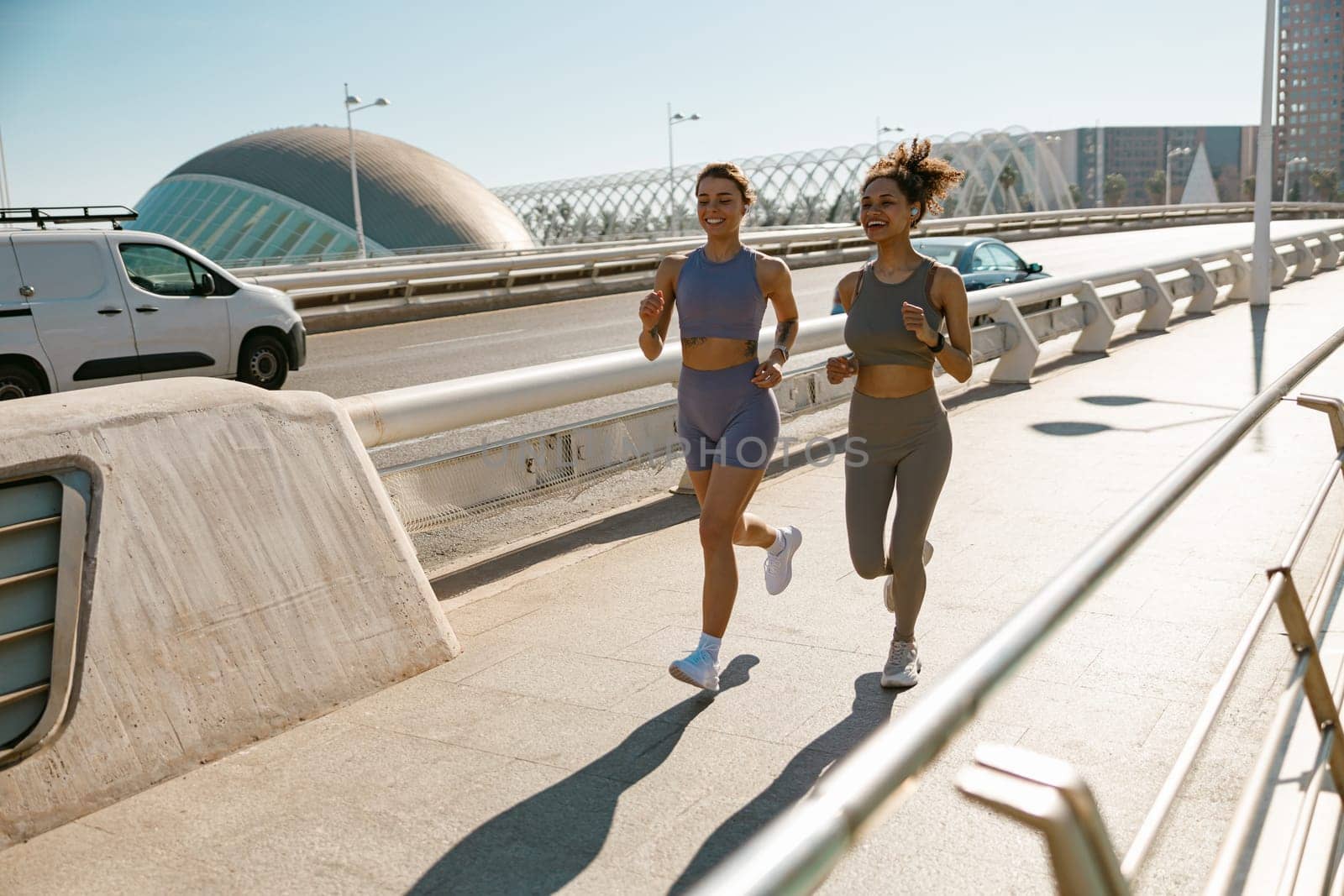 Two active women athlete running side by side along an outdoor track on modern buildings background