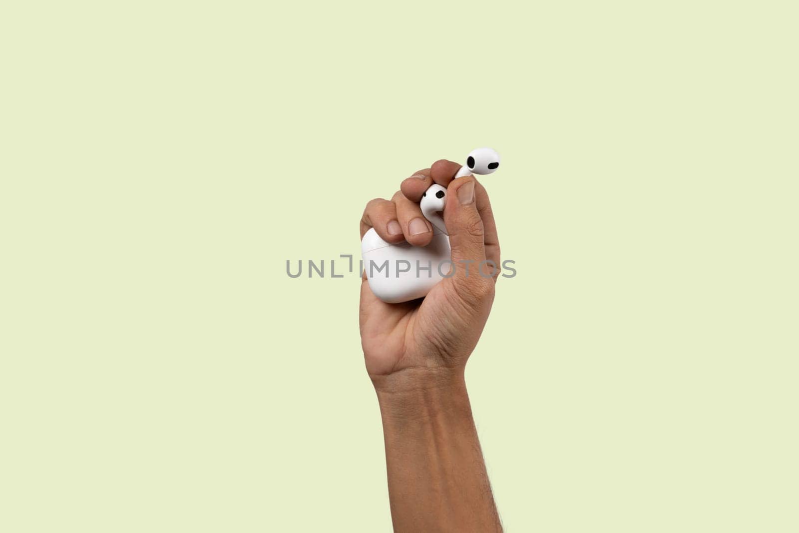 Male hand holding wireless headphones isolated on light green background. High quality photo