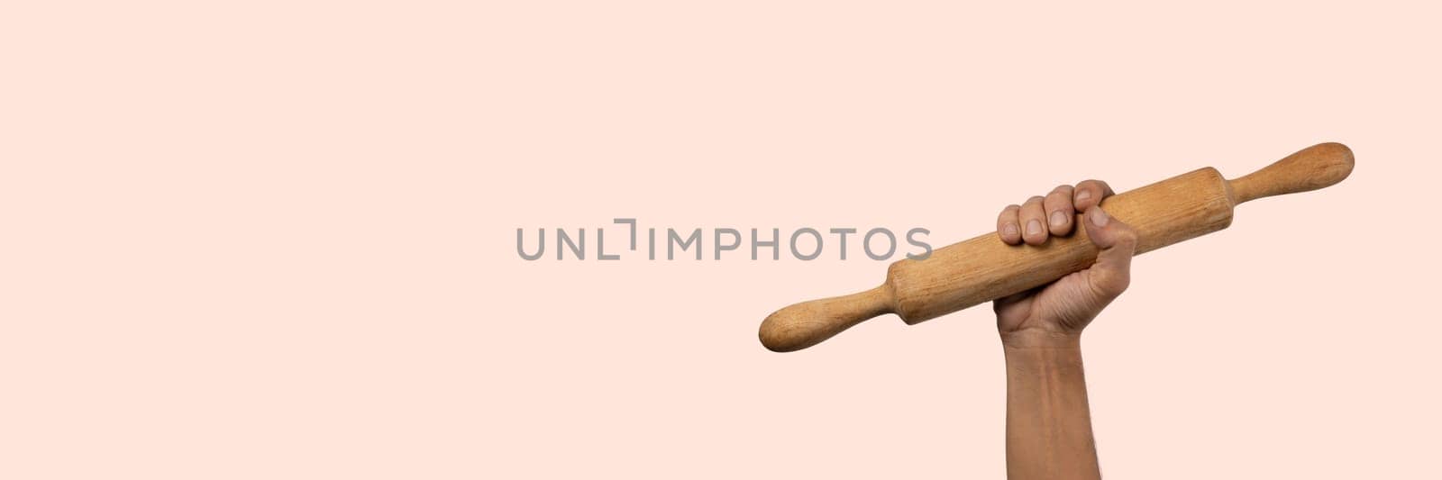 Hand holding a wooden rolling pin isolated on light pink banner background by TropicalNinjaStudio