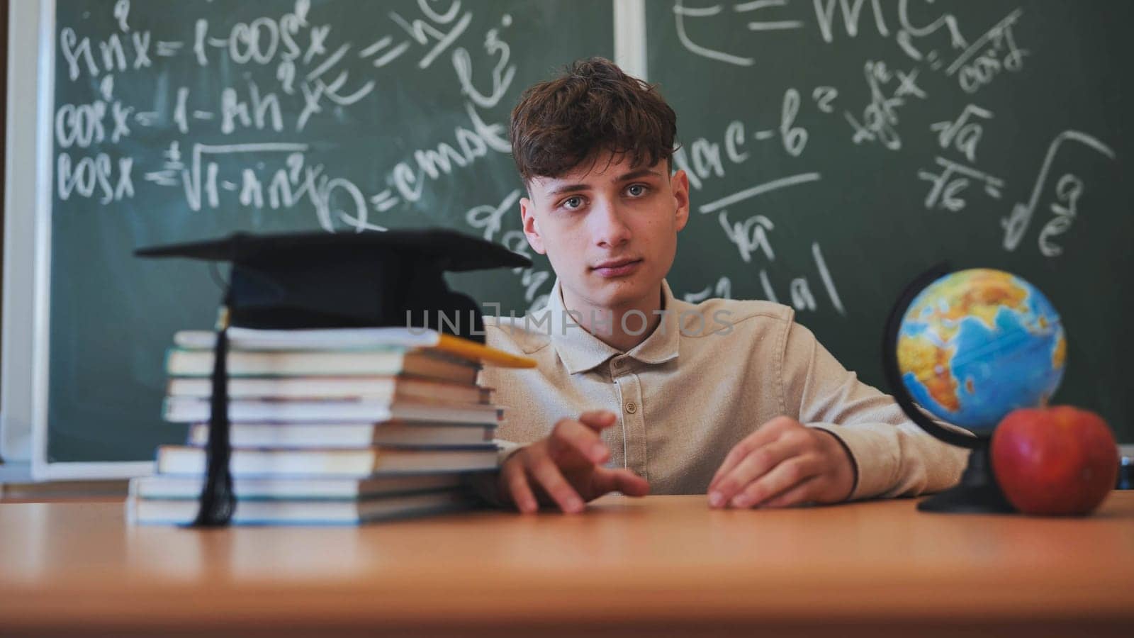 Portrait of a high school student against a background of blackboard, globe and books with cap