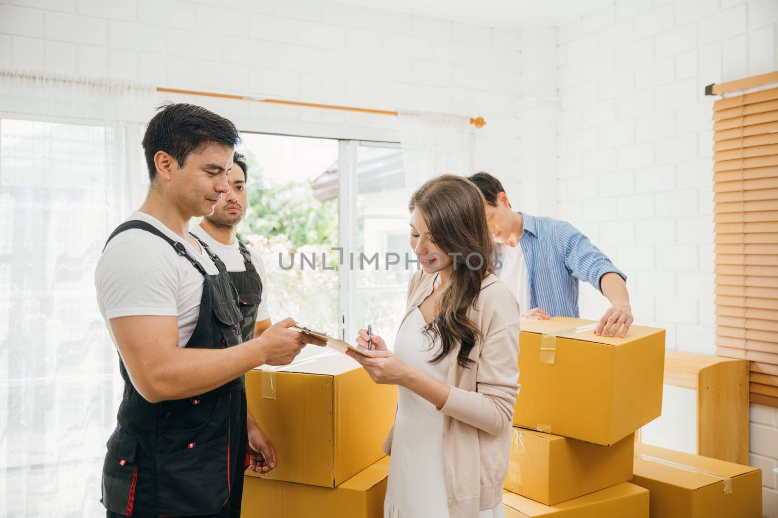 Family reviews moving checklist worker holds a delivery box. Professional movers ensure a successful home relocation. Teamwork and efficient moving displayed. Movind Day to New home by Sorapop