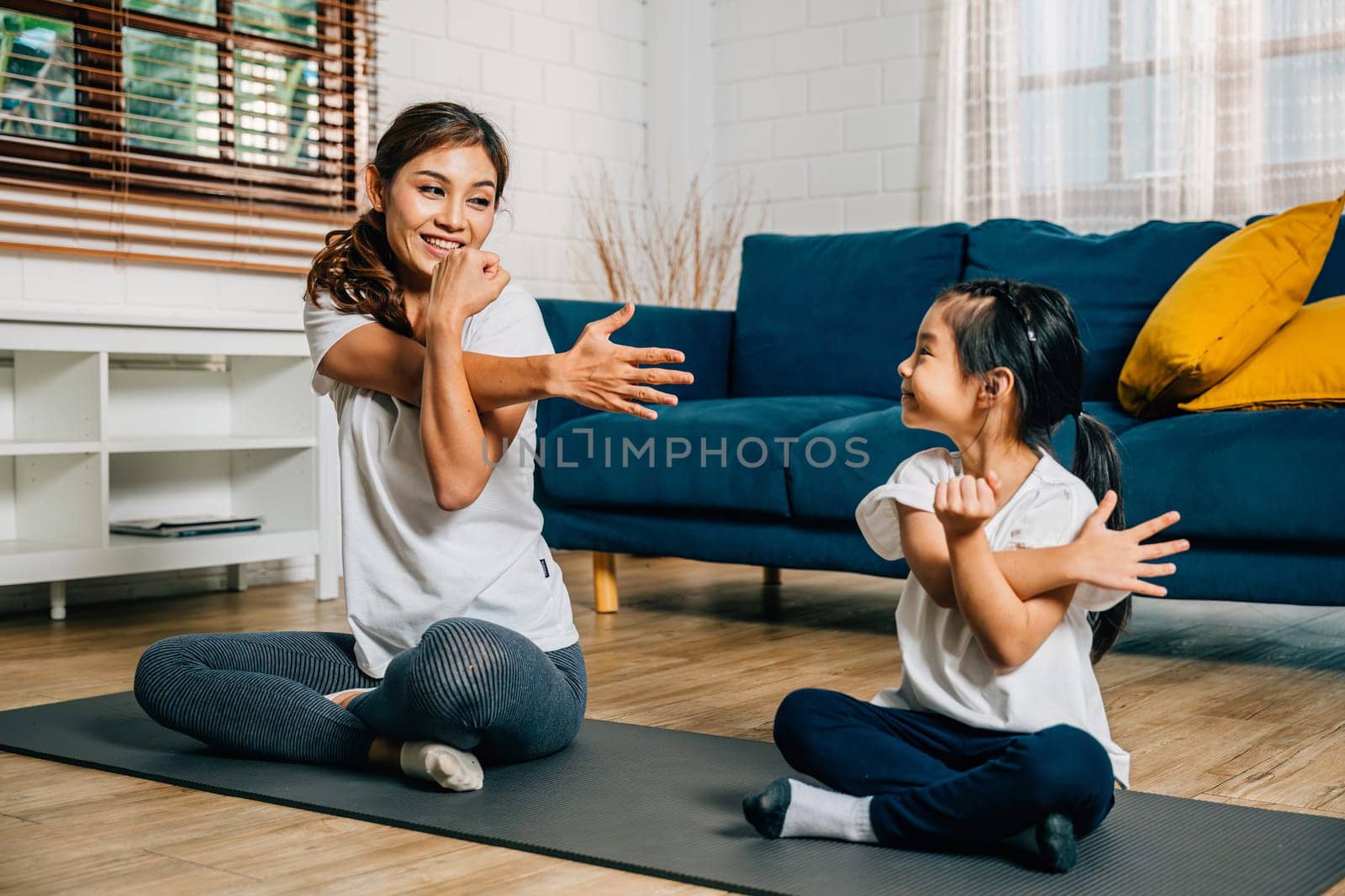In the gym center a mother supports her daughter in stretching and yoga exercises by Sorapop