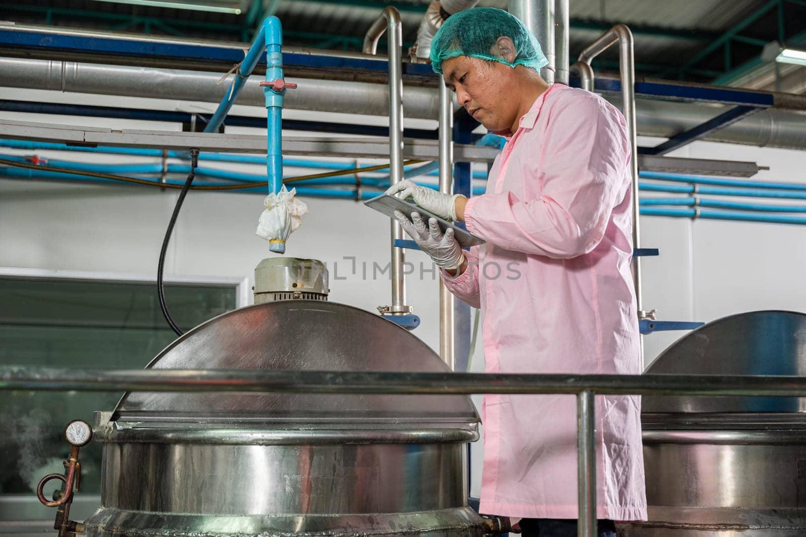 Worker using tablet in beverage factory oversees soda water filling by Sorapop