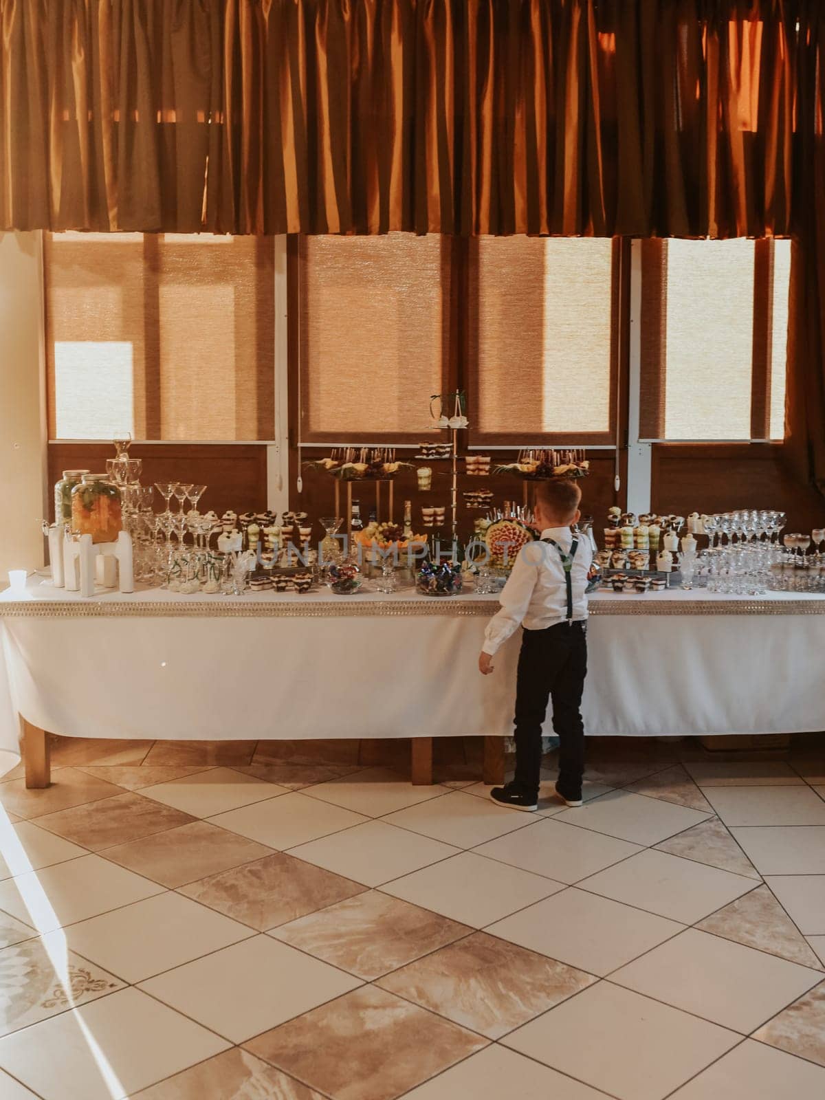 Boy stand eating near catering wedding buffet for events. Beautifully decorated catering banquet table food snacks and appetizers with sandwich. decorated catering banquet table burgers profiteroles