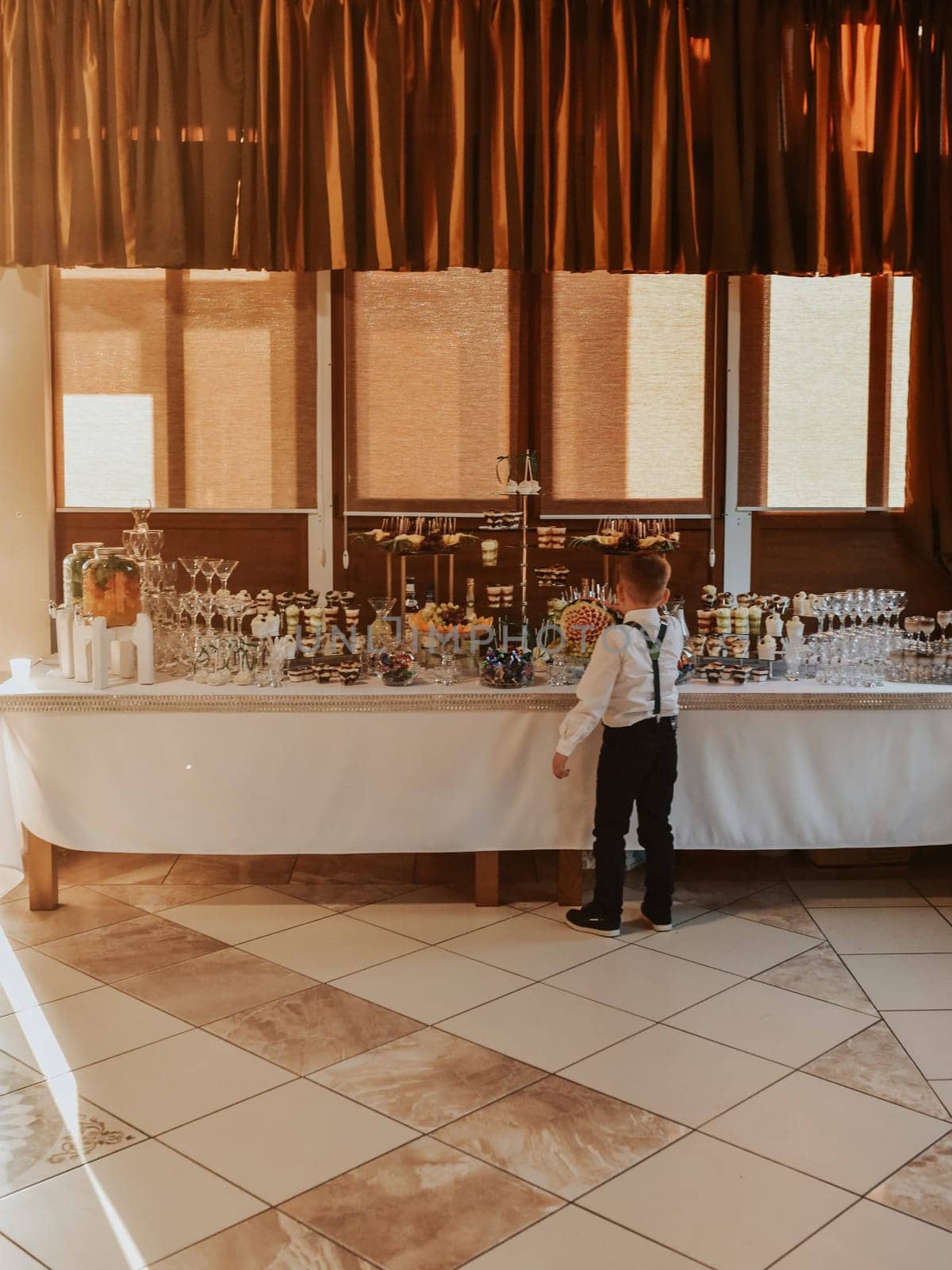 Boy stand eating near catering wedding buffet for events. Beautifully decorated catering banquet by AndriiDrachuk