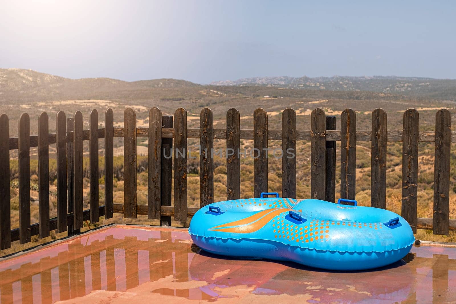 Blue inflatable wheel against background of wooden fence and nature.